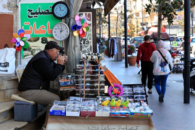 Salah Nasab, a Lebanese street vendor who also sells and repairs clocks, sits next of two clocks that show different times in Lebanon, in the southern port city of Sidon. AP