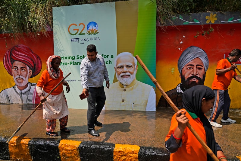 Municipal workers wash a side walk near a billboard featuring Indian Prime Minister Narendra Modi and wall paintings of Indian freedom fighters ahead of this week's summit of the Group of 20 nations, in New Delhi, India. AP Photo