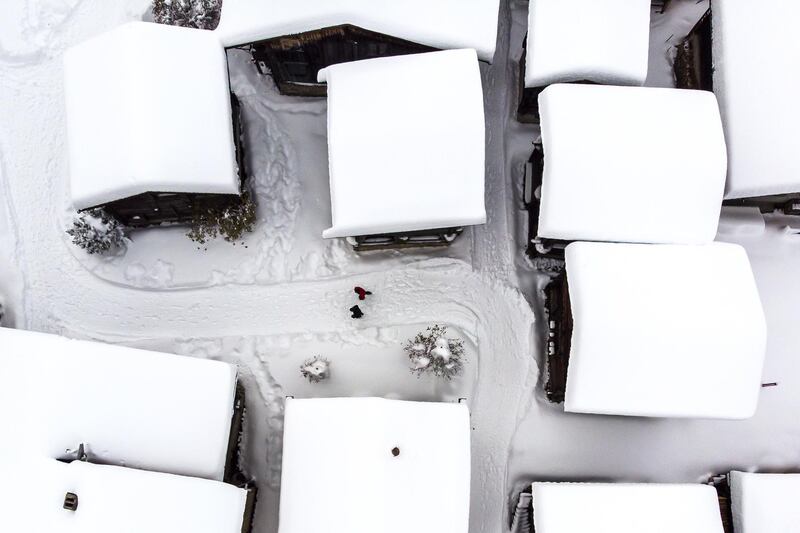 A picture taken with a drone shows a person walking between chalets covered with fresh snow in Bellwald, Switzerland.  EPA