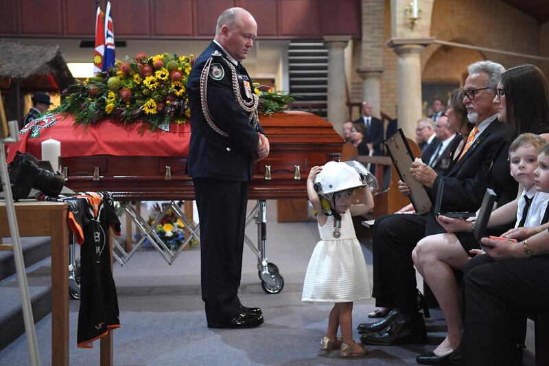 Rural Fire Service Commissioner Shane Fitzsimmons looks at Charlotte O'Dwyer, daughter of New South Wales  Rural Fire Service volunteer Andrew O'Dwyer, wearing her father's helmet during a funeral at Our Lady of Victories Catholic Church in Horsley Park, Sydney. EPA