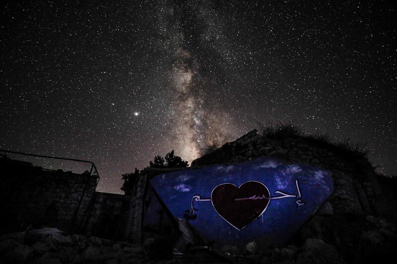 This long-exposure picture taken shows a view of the Milky Way galaxy rising in the sky above a graffiti painted on the rubble of a building the name of the town of Ihsim, in Syria's rebel-held northwestern Idlib province.  AFP