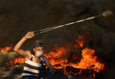 A protester hurls stones while others burn tires near the fence of the Gaza Strip border with Israel, during a protest east of Gaza City, Friday, Sept. 14, 2018. Gaza health officials say 3 Palestinians, including 12-year-old boy, were killed by Israeli army fire in protests along Gaza's perimeter fence. (AP Photo/Adel Hana)