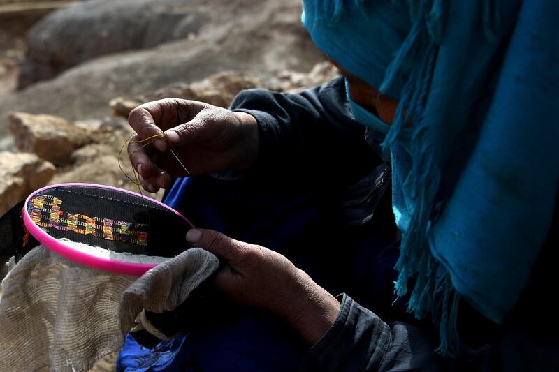 A Hazara woman sews outside a cave where she lives with her family at Tak Darakht village on the outskirts of Bamiyan province on March 6, 2021. (Photo by WAKIL KOHSAR / AFP)