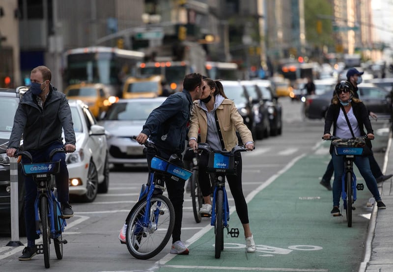 People biking down a road kiss in Manhattan, New York on April 27, 2021. Americans vaccinated against Covid-19 no longer need to mask up outdoors when there is no crowd, President Joe Biden said, before celebrating by taking his first short walk at the White House without the face covering. / AFP / Angela Weiss
