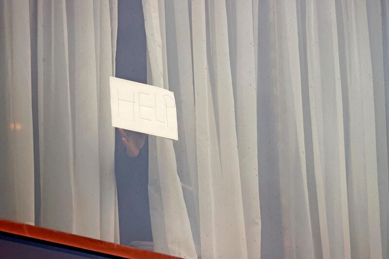 A traveller holds up a 'help' sign at a window during mandatory hotel quarantine in a Radisson Blu hotel. AFP