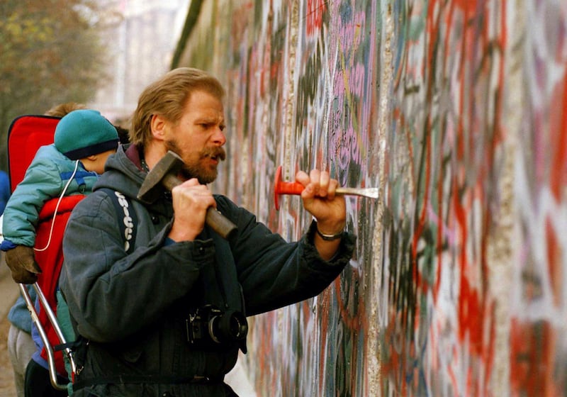 A sight-seeing West Berliner carries his baby and uses a hammer and chisel to carve out a piece of the Berlin Wall. Many souvenir hunters come to the Berlin to break pieces off the crumbling wall. AP Photo