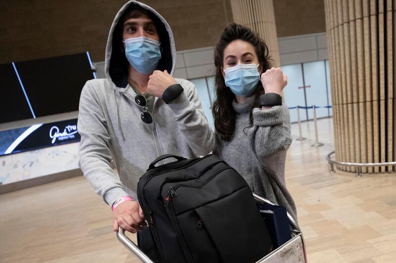 Israeli travelers hold up electronic monitoring bracelets they are required to wear after returning from abroad at the Ben Gurion airport near Tel Aviv, Israel, Monday, March 1, 2021. The bracelets are being tested in a pilot program that will allow people to go into mandatory quarantine at home, instead of state-run hotels, while authorities can ensure they do not violate coronavirus restrictions. (AP Photo/Sebastian Scheiner)