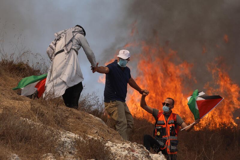 Palestinian protesters help each other seek cover after a tear gas grenade has been thrown at them during clashes after a demonstration against Israel's settlements in the village of Asera near the northern West Bank city of Nablus. EPA