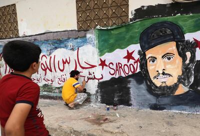 TOPSHOT - A child watches as a local artist works on a mural painting showing the late Syrian rebel fighter Abdel-Basset al-Sarout in the town of Binnish in the jihadist-held northern Idlib province on June 8, 2019. The Syrian goalkeeper turner rebel fighter who starred in an award-winning documentary died of his wounds today aged 27 after fighting regime forces in northwest Syria, a monitor and his faction said.
Al-Sarout was a goalkeeper from the central city of Homs, who became its most popular singer of protest songs after Syrian uprising broke out in March 2011.
 / AFP / OMAR HAJ KADOUR
