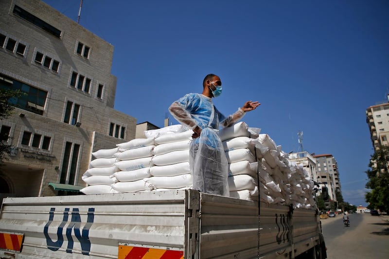 A worker of the United Nations Relief and Works Agency for Palestine Refugees (UNRWA), clad in mask and protective gear due to the COVID-19 coronavirus pandemic, stands in the back of a truck delivering food aid to families in need in Gaza City on September 15, 2020. (Photo by Mohammed ABED / AFP)