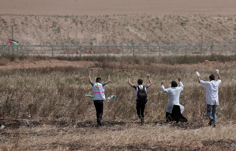 Palestinian medics raise their hands toward the fence to evacuate a wounded youth during clashes with Israeli troops along Gaza's border with Israel, Friday, April 13, 2018. Thousands of Palestinians staged a mass protest along Gaza's sealed border with Israel on Friday, some burning Israeli flags, and Israeli soldiers fired tear gas and live bullets from across the border fence. (AP Photo/Adel Hana)