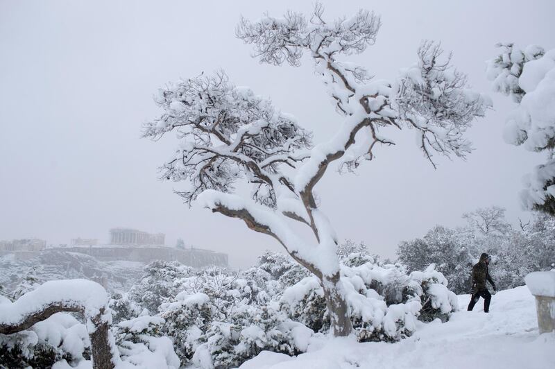 A man walks on Filopappou Hill in Athens as snow falls, with the ancient Acropolis and the Parthenon in the background. AP