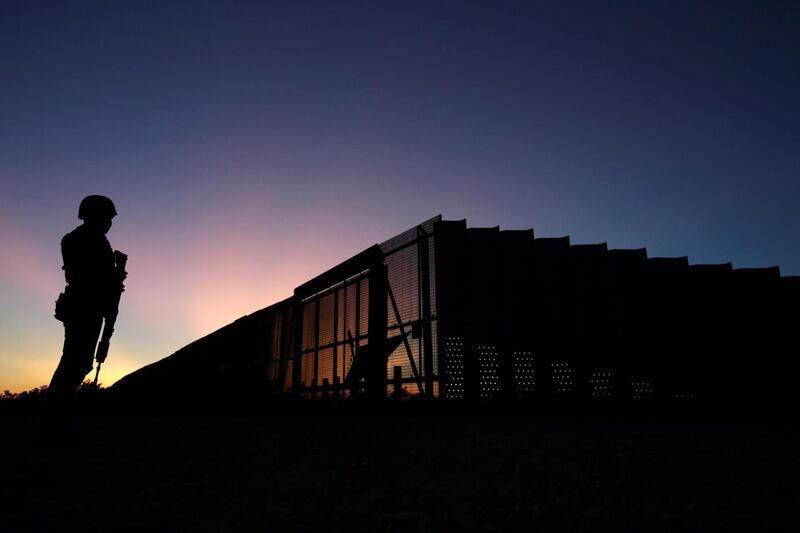 A soldier assigned to the National Guard is silhouetted while keeping watch near a section of the border fence between Mexico and United States. Reuters