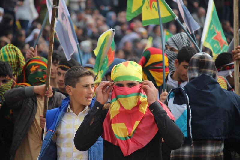 A young man uses a PKK flag to conceal his face - and the flag of the Syrian-Kurdish YPG militia as a bandana to cover his head - as he marches at Nowruz celebrations in Diyarbakir on March 21, 2016. Josh Wood for The National