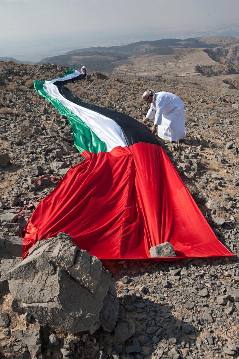 Ras al Khaimah, December 1, 2011 - Brothers Waleed, foreground and Ahmed Bin Shaiban al Hebsi, background, puts rocks on a 40 meter flag to keep it in place on the top of Jebel Janas near Ras al Khaimah City, Ras al Khaimah, December 1, 2011. (Jeff Topping/The National)