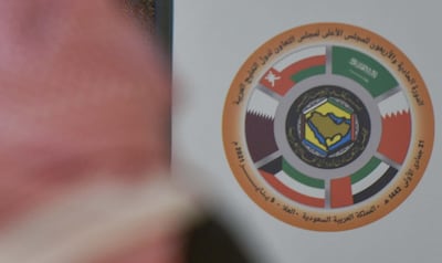 A Saudi journalist is pictured in front of the logo of the Gulf Cooperation Council (GCC) and the Qatari national flag at the media centre ahead of the 41st summit in the city of al-Ula in northwestern Saudi Arabia on January 5, 2021. - Saudi Arabia will reopen its borders and airspace to Qatar, US and Kuwaiti officials said, a major step towards ending a diplomatic rift that has seen Riyadh lead an alliance isolating Doha. The bombshell announcement came on the eve of GCC annual summit in the northwestern Saudi Arabian city of Al-Ula, where the dispute was already set to top the agenda. (Photo by FAYEZ NURELDINE / AFP)