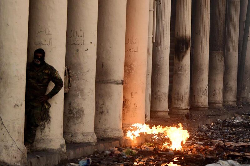 A member of Iraqi anti-riot police forces takes cover during clashes with anti-government protesters at the Al Rasheed street in central Baghdad.  EPA