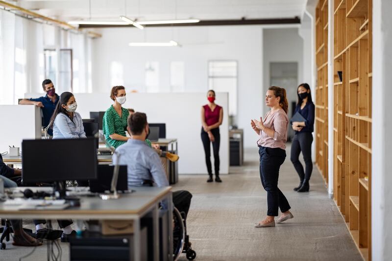 Female entrepreneur explaining new working strategies to team post-pandemic reopen. Business professionals having a meeting in the creative office after lockdown.