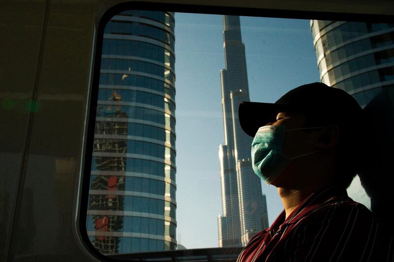 FILE - In this April 26, 2020, file photo, a commuter wearing a face mask to help curb the spread of the coronavirus, sleeps aboard the driverless Metro as it passes the Burj Khalifa, the world's tallest building, in Dubai, United Arab Emirates. Gulf Arab states on Thursday, Feb. 4, 2021 launched new restrictions over fears of the coronavirus resurging across their countries. (AP Photo/Jon Gambrell, File)