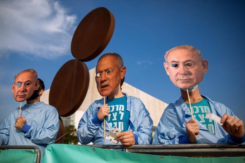 Israeli demonstrators hold masks depicting Israeli Prime Minister Benjamin Netanyahu and Israeli Defense Minister Benny Gantz during a protest against a parliamentary vote to dissolve the Knesset and send the country to its fourth elections in two years while it still hasn't approved a national budget for 2020, in Tel Aviv, Wednesday, Dec. 2, 2020. (AP Photo/Oded Balilty)