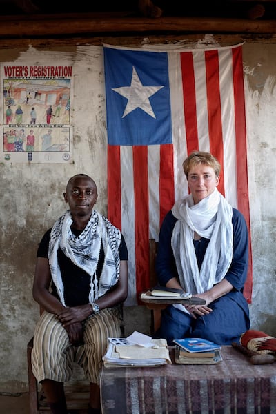 Emma Thompson and her adopted son Tindyebwa Agaba, who is known as Tindy, sit infront of the Liberian flag that hangs in Maime Smith's front porch in Zannah village, Monserrado county, Liberia.