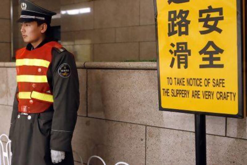 A security guard stands next to a sign which reads in English, "To Take Notice of Safe The Slippery Are Very Crafty", at the entrance of a Beijing shopping mall.