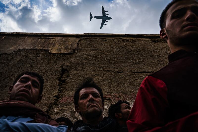 A military transport plane flies over relatives and neighbours of the Ahmadi family as they gather around an incinerated husk of a vehicle destroyed by a US drone strike in Kabul. By Marcus Yam. Los Angeles Times/EPA