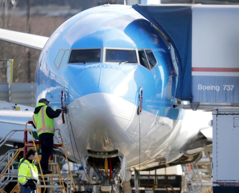 FILE- In this March 13, 2019, file photo a worker stands on a platform near a Boeing 737 MAX 8 airplane being built for TUI Group at Boeing Co.'s Renton Assembly Plant in Renton, Wash. Boeing is cutting production of its grounded Max airliner this month to focus on fixing flight-control software and getting the planes back in the air. The company said Friday, April 5, that starting in mid-April it will cut production of the 737 Max from 52 to 42 planes per month. (AP Photo/Ted S. Warren, File)