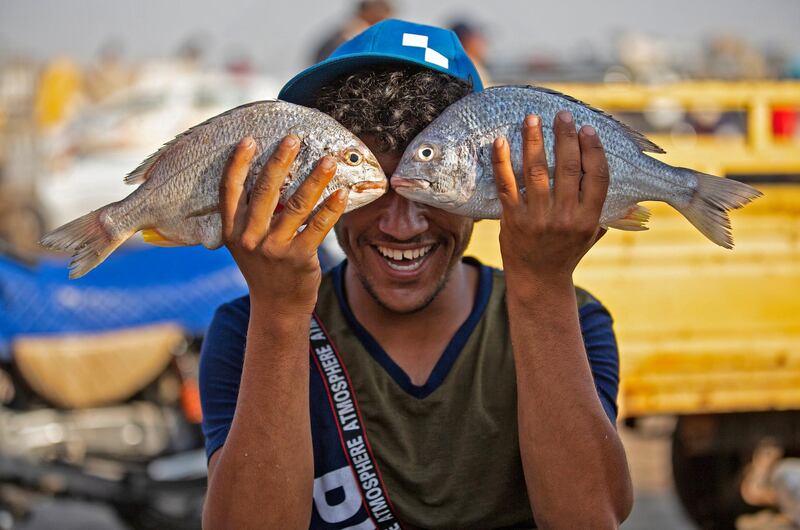 A youth poses while holding two fishes before his face in Iraq's southern port city of al-Faw, 90 kilometres south of Basra near the Shatt al-Arab and the Gulf, on May 18, 2020. - In Iraq, a national lockdown to halt the COVID-19 coronavirus pandemic has found some unexpected fans: local businesses who no longer have to compete with Turkish, Iranian or Chinese imports. Those countries, as well as Saudi Arabia, Jordan and Kuwait, typically flood Iraqi markets with inexpensive products at prices local producers can't compete with. (Photo by Hussein FALEH / AFP)