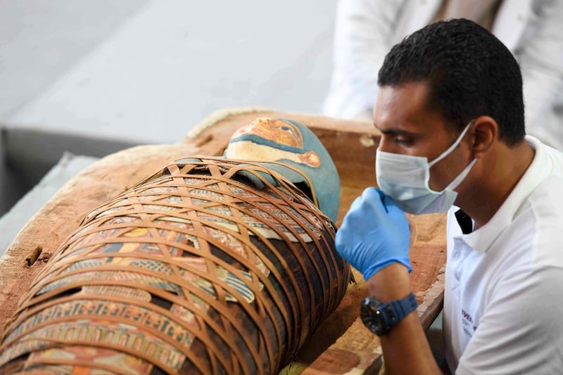 Archaeologists inspect a mummy, wrapped in a burial shroud adorned with brightly coloured hieroglyphics pictorials, during the unveiling of an ancient treasure trove of more than a 100 intact sarcophagi. AFP