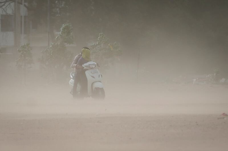 A couple ride a scooter amid dust stirred up by strong wind in Ahmedabad. Reuters