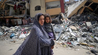 A Palestinian woman holds her daughter as she walks past destroyed buildings in the north of Al Nusairat refugee camp, southern Gaza Strip, 29 April 2024. EPA