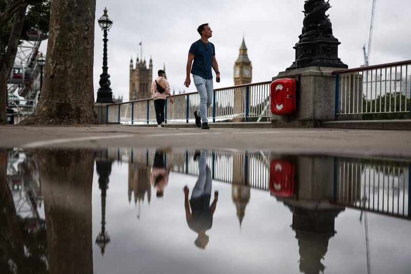 A pedestrian walks on the Southbank by the river Thames, in central London, on July 27, 2023 as he is reflected in a puddle with Elizabeth Tower, commonly called Big Ben, on a gloomy summer day.  (Photo by HENRY NICHOLLS  /  AFP)