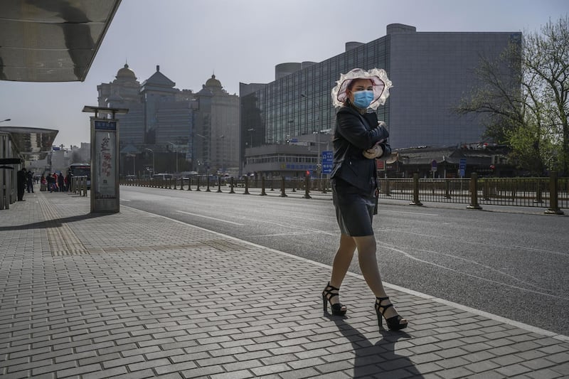 A Chinese woman wears a protective mask as she waits at a bus stop before three minutes of silence to mark the country's national day of mourning for Covid-19 near Beijing Railway Station. Getty Images