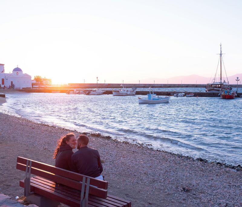 A couple sit by the sea during sunset at the Old Port in Mykonos. Photographer: Loulou D'Aki/Bloomberg