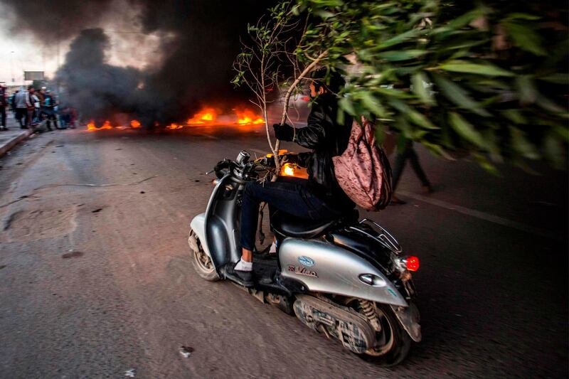 An Iraqi protester holds a broken tree as he drives a scooter towards other protesters blocking the road with a tire fire, during a demonstration against corruption and lack of services in the southern city of Basra. AFP