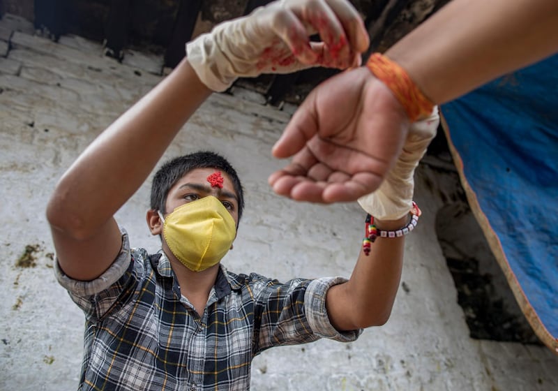 A young child priest ties a sacred thread, known as Janai, around the wrist of a devotee during the Janai Purnima festival, amid coronavirus pandemic, at the Bagmati River in Kathmandu, Nepal. EPA