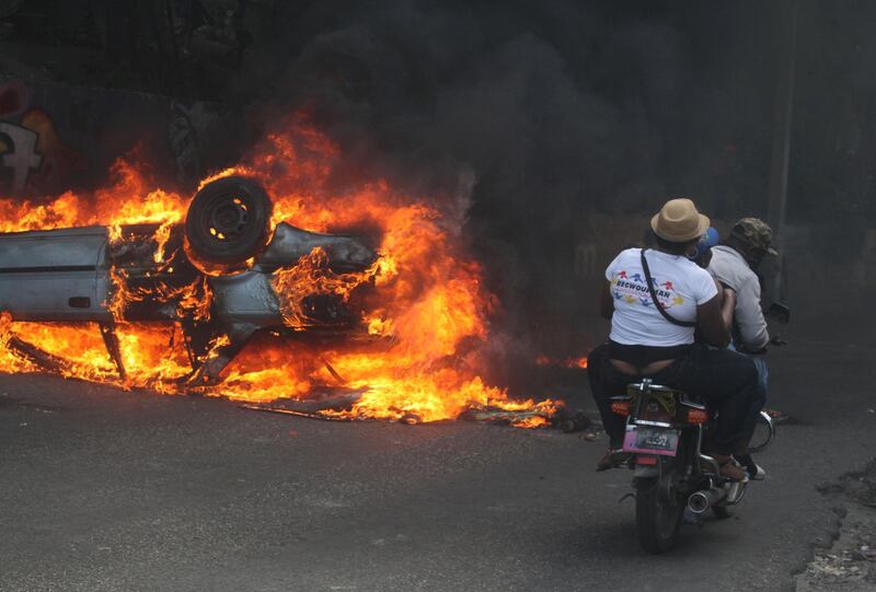 People on a motorcycle ride near a burning car. Reuters