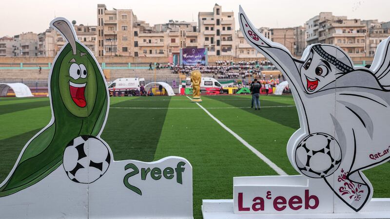 The mascot of the Camps World Cup, depicted as an olive called Hareef (expert), is presented with the mascot of the Qatar World Cup, La'eeb, during the event's opening ceremony in Idlib