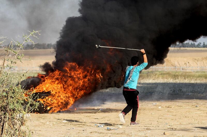A Palestinian youth swings a sling shot during clashes after a demonstration near the border with Israel, east of Khan Yunis in the southern Gaza Strip, on April 01, 2018. / AFP PHOTO / SAID KHATIB