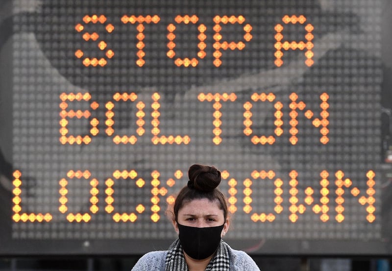 A woman wearing a face mask or covering due to the COVID-19 pandemic, walks near an electronic road sign reading "Stop a Bolton Lockdown" in Bolton town centre, northwest England on October 7, 2020. The UK government recently imposed tougher coronavirus restrictions in northwest England, as it voiced fears about rising infection rates among younger people. / AFP / Oli SCARFF
