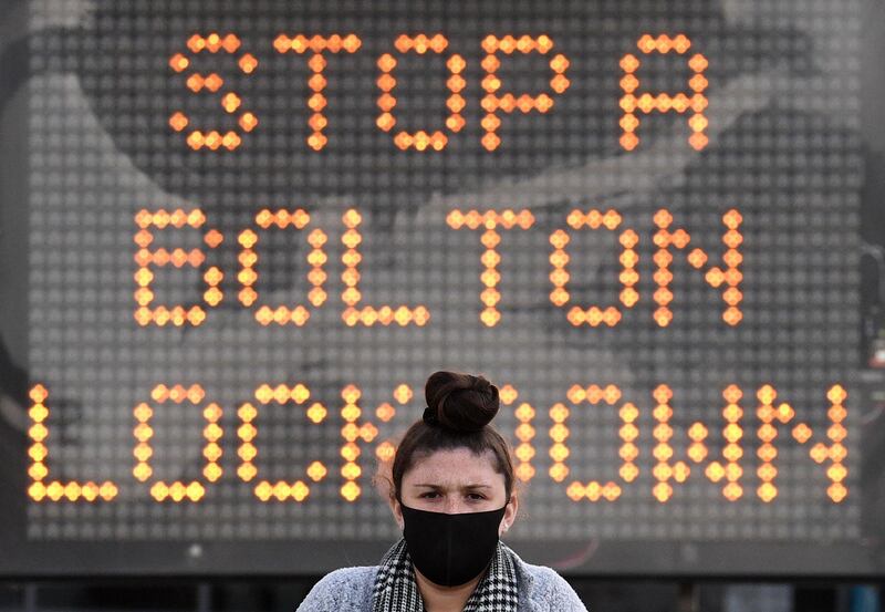 A woman wearing a face mask or covering due to the COVID-19 pandemic, walks near an electronic road sign reading "Stop a Bolton Lockdown" in Bolton town centre, northwest England on October 7, 2020. The UK government recently imposed tougher coronavirus restrictions in northwest England, as it voiced fears about rising infection rates among younger people. / AFP / Oli SCARFF
