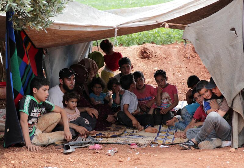 FILE PHOTO: A displaced Syrian farmer holds his daughter as he sits with other family members in an olive grove in the town of Atmeh, Idlib province, Syria, May 16,  2019. REUTERS/Khalil Ashawi/File Photo