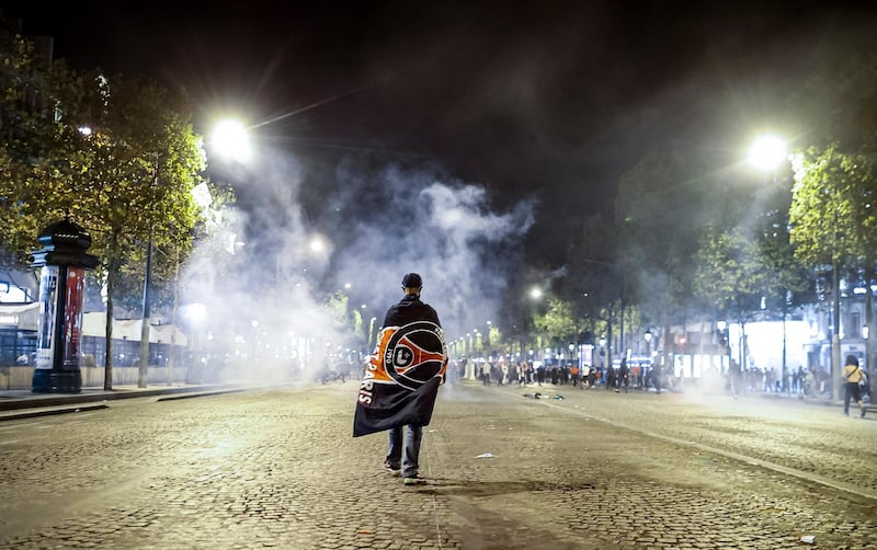 A Paris Saint Germain supporter walks through a cloud of teargas on the Champs Elysees. EPA