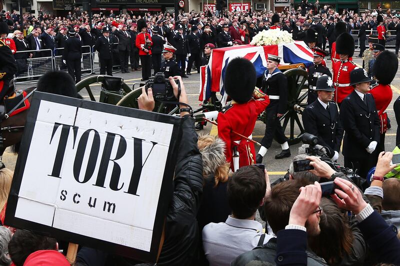 LONDON, ENGLAND - APRIL 17:  A protest sign as the coffin is carried on a horse drawn gun carriage during the Ceremonial funeral of former British Prime Minister Baroness Thatcher at Ludgate Hill on April 17, 2013 in London, England. Dignitaries from around the world today join Queen Elizabeth II and Prince Philip, Duke of Edinburgh as the United Kingdom pays tribute to former Prime Minister Baroness Thatcher during a Ceremonial funeral with military honours at St Paul's Cathedral. Lady Thatcher, who died last week, was the first British female Prime Minister and served from 1979 to 1990.  (Photo by Clive Rose/Getty Images) *** Local Caption ***  166796408.jpg