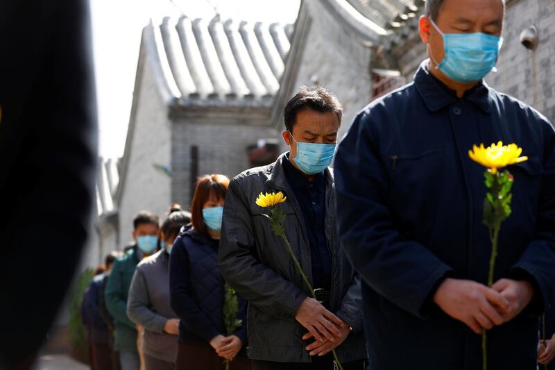 People holding flowers observe a moment of silence at a memorial event in Beijing as China holds a national mourning. cnsphoto via Reuters