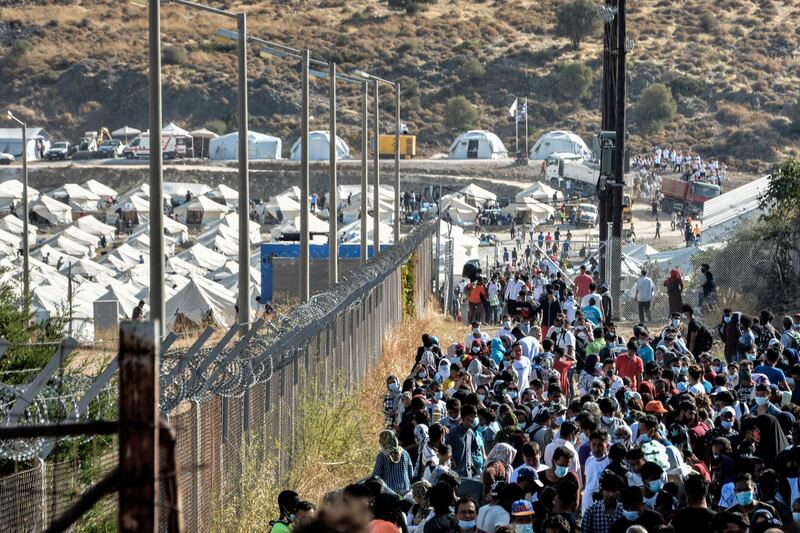 Migrants most of them, wearing face masks against the spread of the new coronavirus, gather outside the temporary refugee camp in Kara Tepe as they wait to depart from Lesbos for mainland Greece, Monday, Sept. 28, 2020. About 700 people will leave later today, twenty days after successive fires that started before dawn on Sept. 9, devastating the Moria refugee camp and making more than 12,000 inhabitants homeless during a COVD-19 lockdown. (AP Photo/Panagiotis Balaskas)