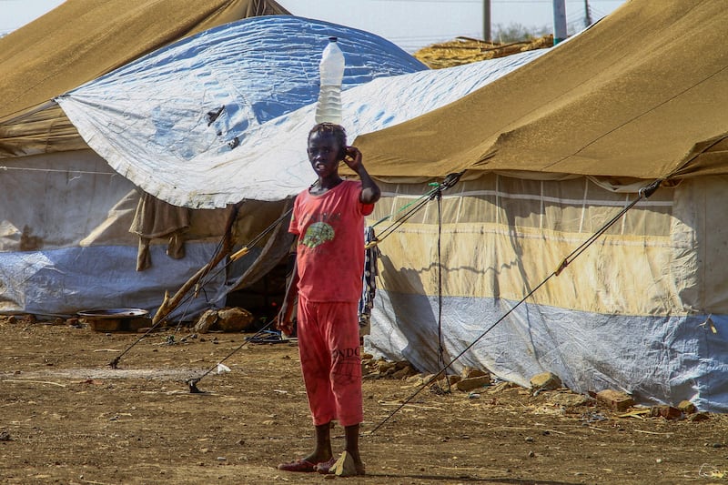 A picture taken on March 20, 2024, shows a displaced girl carrying a water bottle on her hear walking among tents at a camp in southern Gadaref state for people who fled Khartoum and Jazira states in war-torn Sudan.  After nearly a year of war, Sudan is suffering one of the worst humanitarian crises in recent history, the United Nations warned on March 20, slamming the international community for its lack of action.  (Photo by AFP)