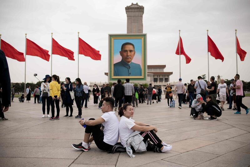 A couple sit back-to-back past a portrait of nationalist leader Sun Yat-sen in Tiananmen Square, Beijing. Nicolas Asfouri / AFP Photo