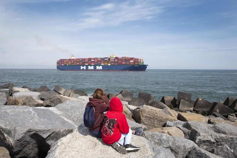 Two people sit on rocks as the world largest container vessel HMM Algeciras approach the port of Rotterdam. AFP